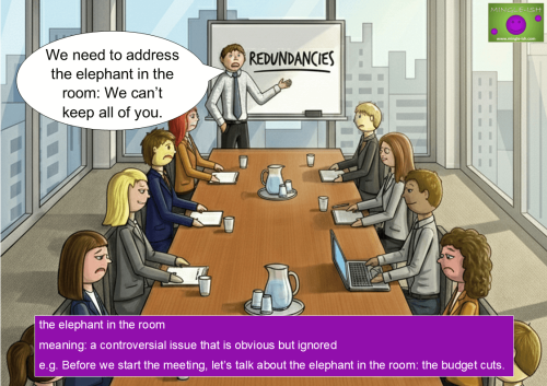 An illustration of a tense office meeting where a speaker uses the idiom "the elephant in the room" to announce job redundancies.